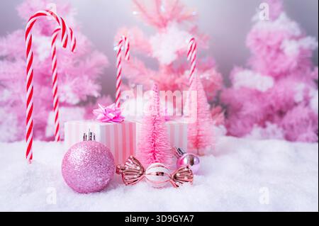 Una composizione natalizia rosa natalizia con scatole regalo rosa pastello, ornamenti scintillanti, decorazioni di caramelle e alberi in miniatura smerigliati. Foto Stock