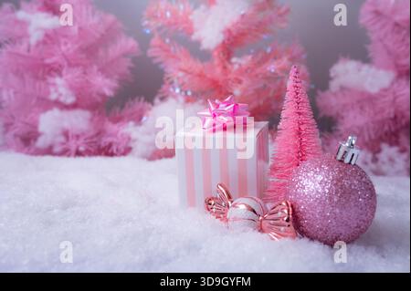 Una composizione natalizia rosa natalizia con scatole regalo rosa pastello, ornamenti scintillanti, decorazioni di caramelle e alberi in miniatura smerigliati. Foto Stock