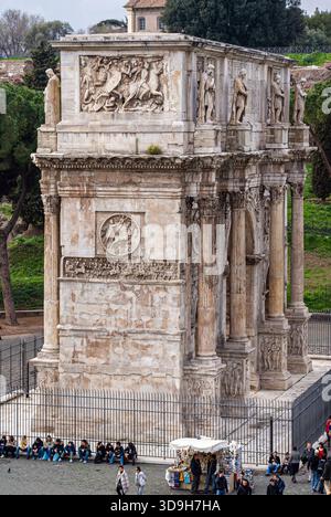 Vista laterale ravvicinata dell'Arco di Costantino, che mette in evidenza i rilievi scolpiti, le colonne e le statue superiori. Le persone e uno stallo dei fornitori sono visibili a Foto Stock