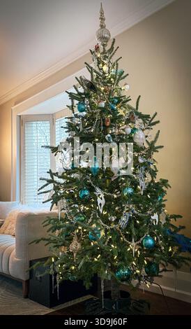 Albero di Natale naturale completamente decorato in un ambiente caldo con luci e ornamenti. Foto Stock