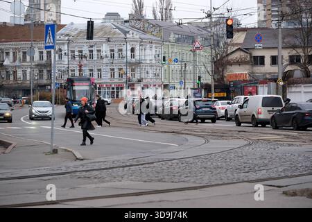 Le persone attraversano la strada mentre le auto aspettano al semaforo nel centro città. Kiev, Ucraina. 5 dicembre 2025. Foto Stock
