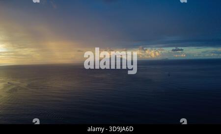 Turbolento crepuscolo: Spettacolare mare e cielo con sagome di Distant Island al tramonto Foto Stock