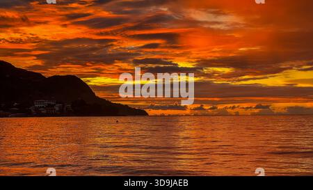 Toni caldi del tramonto riflessi sulla superficie dell'oceano con la silhouette dell'isola Foto Stock