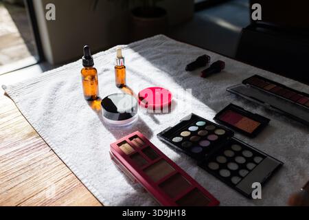 Prodotti cosmetici appoggiati su un asciugamano bianco sul tavolo vicino alla finestra aperta, fascio diagonale di emissione della luce solare Foto Stock