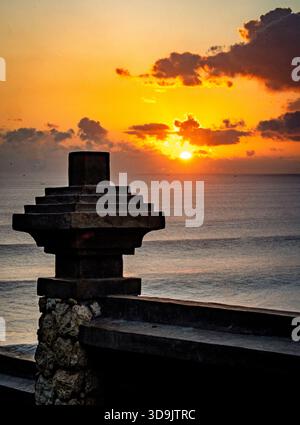 Silhouette di una struttura in pietra contro un vibrante tramonto sull'oceano. Foto Stock