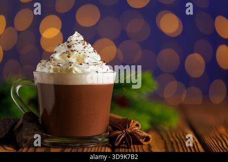 Cioccolata calda con panna montata in tazza di vetro su sfondo blu di luci bokeh scintillanti della ghirlanda Foto Stock
