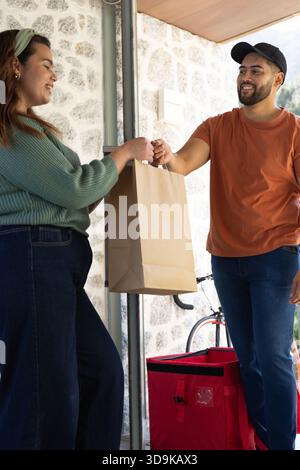 Diversi addetti alle consegne che consegnano un sacchetto di carta al cliente sul portico coperto accanto al sacchetto rosso e alla bicicletta Foto Stock