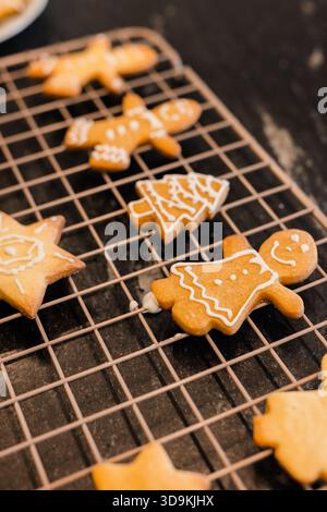 Griglia di raffreddamento a filo appoggiata su un bancone scuro che regge l'albero stellare di pan di zenzero e forme umane ghiacciate di bianco Foto Stock
