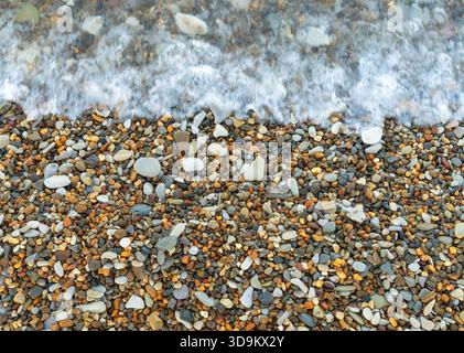 Il lavaggio delle onde marine su una riva coperta di ciottoli multicolori Foto Stock