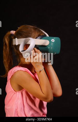 Bambino che indossa il visore per realtà virtuale e tiene in mano i controller di movimento mentre interagisce con contenuti VR immersivi in ambiente studio Foto Stock