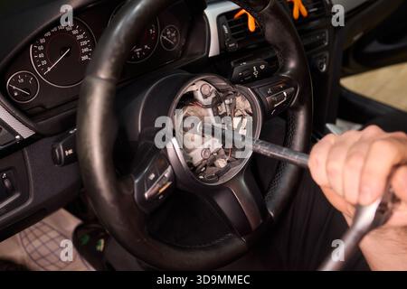 Riparazione dettagliata dell'auto, colpo di mano mirato che ripristina con attenzione il componente dello sterzo del veicolo, lavoro di precisione sul volante del veicolo con attrezzi in Foto Stock