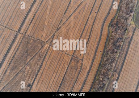 Ripresa con droni che cattura l'intricato schema lineare del campo coltivato attraversato da cingoli per macchinari pesanti. La consistenza calda del terreno è leggermente disturbata da piccole tracce di conchiglie, creando uno sfondo astratto unico Foto Stock