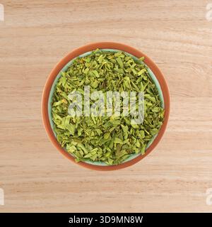 Tagliare il dragoncello in una piccola ciotola di terracotta su una vista dall'alto del ripiano in legno. Foto Stock