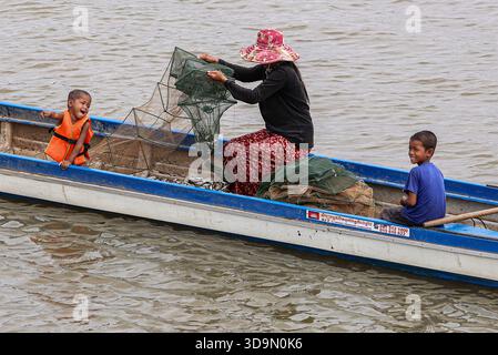 Fiume Tonle SAP, Cambogia. 6 dicembre 2025. I pescatori cambogiani recuperano le loro trappole quadrate di pesce dalle tradizionali barche in legno sul fiume Tonle SAP, approfittando della migrazione stagionale del pesce mentre il lago continua a drenare verso il fiume Mekong dopo l'inversione annuale del flusso all'inizio di ottobre. Durante questo periodo di deflusso, un gran numero di piccole specie di acqua dolce si spostano a valle in scuole dense. Questo raro fenomeno idrologico crea le condizioni ideali per le comunità di pescatori locali che si affidano pesantemente a questa stagione per la raccolta di pesci d'acqua dolce. Crediti: Kevin Izorce/Alamy Live News Foto Stock