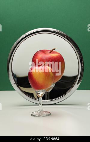 Natura morta con specchio ingrandente e frutta. Specchio concavo e mela su sfondo verde. Foto con grande profondità di campo. Foto Stock