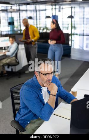 Diversi colleghi che collaborano in un ufficio open space in un moderno spazio di lavoro utilizzando laptop e tablet Foto Stock