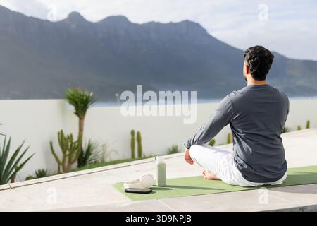 Uomo indiano che meditava sul tappetino da yoga in terrazza con cuffia per bottiglia d'acqua, spazio fotocopie Foto Stock