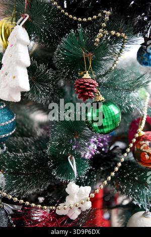 Un primo piano verticale di un albero di Natale artificiale decorato con un ornamento di alberi bianchi, un baule verde metallizzato e una ghirlanda con perline d'oro. Foto Stock