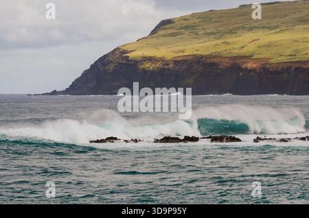 Le onde si infrangono sulle coste rocciose vicino alla collina erbosa, l'Isola di Pasqua. Foto Stock