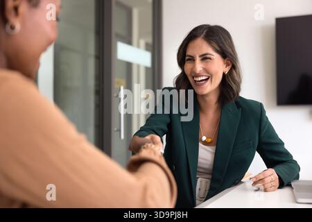 Allegra soddisfatta giovane donna d'affari ispanica che stringe la mano al partner Foto Stock