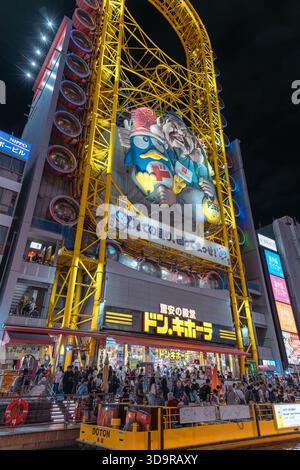 La gigantesca ruota panoramica gialla di Don Quijote e l'enorme cartellone dei cartoni animati illuminano l'affollata passeggiata del vibrante quartiere Dotonbori di Osaka. Foto Stock