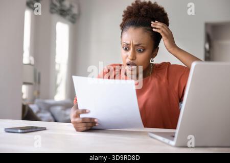 Scioccata ansiosa stressata giovane donna africana che legge una lettera formale Foto Stock