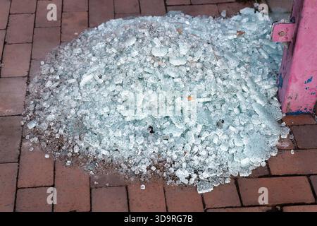 Frammenti di vetro rotti raccolti vicino al palo della fermata dell'autobus in metallo rosa su marciapiedi piastrellati di mattoni rossi, che mostrano danni alle strade urbane. Foto Stock