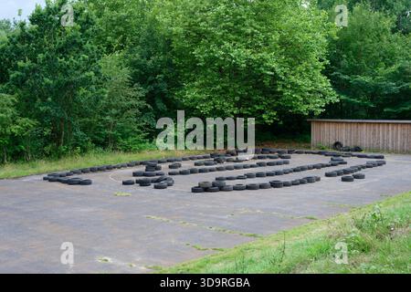 Pista da go-kart all'aperto con barriere per pneumatici circondate da lussureggianti alberi verdi. Foto Stock