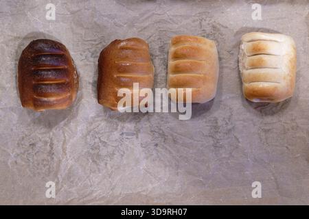 Quattro salsicce cotte nell'impasto si trovano su pergamena rugosa. Ognuna è una tonalità diversa da marrone scuro a chiaro, disposta da sinistra a destra. Foto Stock