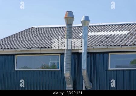 Due camini di metallo sul tetto di un edificio contro un cielo azzurro. I camini hanno diversi design e altezze, con uno che mostra segni di ruggine. La b Foto Stock