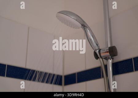 Box doccia in metallo con soffione a pioggia montato che versa acqua in un angolo piastrellato caratterizzato da pareti piastrellate bianche e blu dal moderno design del bagno Foto Stock