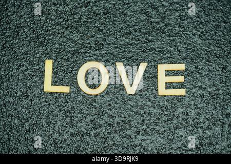 La parola "amore" è formata da lettere di legno poste su un tappetino in gomma nero con una texture sottile, offrendo una presentazione visiva chiara e creativa. Foto Stock