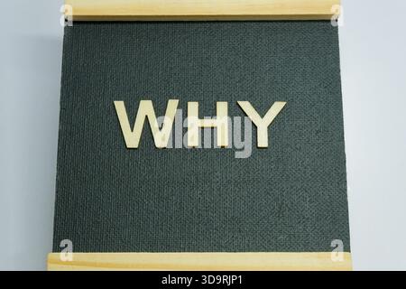 La parola PERCHÉ è chiaramente formata con lettere di legno su un display in tessuto nero. Un pezzo decorativo che suscita curiosità e pensiero critico in ogni sua parte Foto Stock