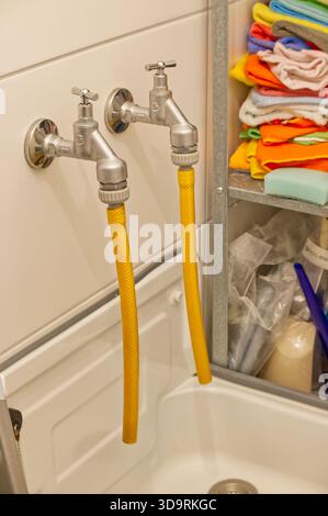 Un armadietto clinico bianco si trova contro la parete con ripiani aperti. Molti panni colorati e spugne sono impilati e piegati per le attività di pulizia, gli organizi Foto Stock