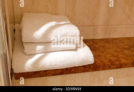 Una piccola sporgenza di pietra accanto alle piastrelle della doccia contiene tre asciugamani di spugna bianca. Grandi, medie e piccole sono piegate in modo ordinato, aggiungendo un tocco di hotel ad un Foto Stock