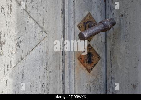 Primo piano di una vecchia porta in legno con una superficie resistente agli agenti atmosferici, con una maniglia in metallo arrugginito e un foro a forma di diamante. Foto Stock