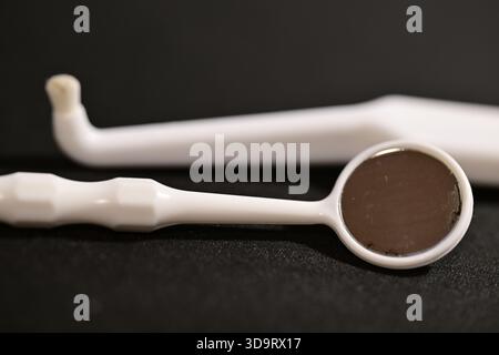 Un primo piano di strumenti dentali, tra cui uno specchio dentale e un esploratore, su uno sfondo scuro. Gli utensili sono bianchi con una superficie riflettente, utilizzati per o. Foto Stock