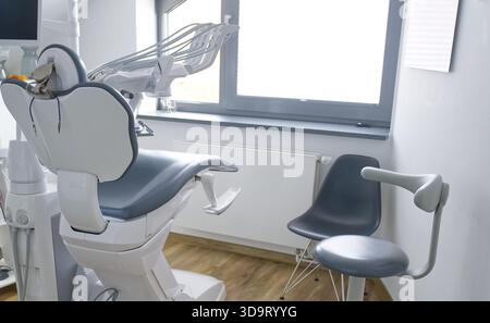 Un moderno studio dentistico con una sedia dentale, una piccola sedia laterale e una grande finestra che consente la luce naturale. Il decor e' minimalista e pulito Foto Stock