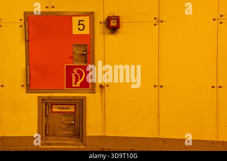 Una parete gialla luminosa con porta di accesso per idranti antincendio e allarme antincendio. La porta è contrassegnata con il numero 5 e include un simbolo di idrante antincendio. T Foto Stock