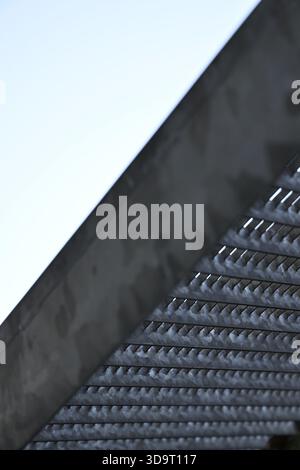 Vista ravvicinata di una moderna struttura architettonica caratterizzata da una superficie testurizzata con linee verticali e un cielo azzurro limpido sullo sfondo. Foto Stock