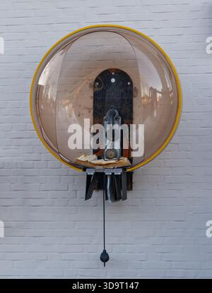Un telefono pubblico retrò particolarmente elegante in una cupola trasparente su una parete, davanti a uno sfondo bianco in mattoni e un vecchio telefono aperto Foto Stock