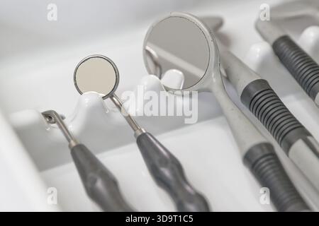 Vista ravvicinata degli strumenti dentali, tra cui specchi ed esploratori, disposti ordinatamente in un vassoio Gli utensili sono in metallo con impugnature in gomma, che ne mostrano l'aspetto Foto Stock