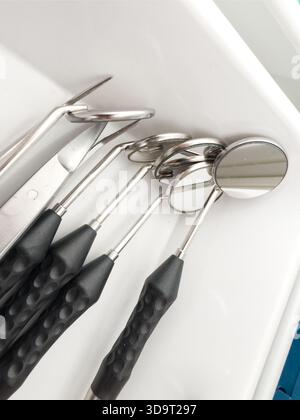 Vista ravvicinata degli strumenti dentali, tra cui specchi ed esploratori, sistemati ordinatamente in un vassoio Gli strumenti sono dotati di teste in metallo lucido e lama testurizzata Foto Stock