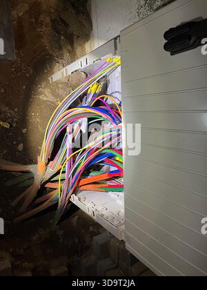 Una vista ravvicinata della scatola di derivazione per telecomunicazioni in fibra ottica con cavi e fili colorati in fibra ottica che emergono da essa, in un ambiente scarsamente illuminato W Foto Stock