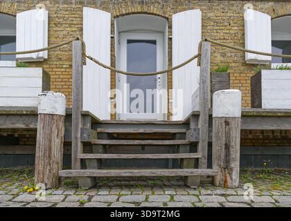 Un'entrata rustica dell'edificio presenta scalini di legno che conducono ad una porta, fiancheggiati da persiane bianche. La facciata e' fatta di mattoni gialli, con un cartello rea Foto Stock
