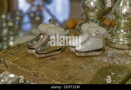 Due ornamenti decorativi per pattinaggio su ghiaccio, uno d'argento e uno bianco, con morbide sommità, posti su una superficie in legno. Lo sfondo sfocato è caratterizzato da un effetto festivo sfocato Foto Stock