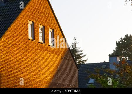 Una vista ravvicinata di una casa in mattoni con tetto inclinato, illuminata dal caldo bagliore del sole che tramonta. La luce del sole proietta ombre sul mattone Foto Stock