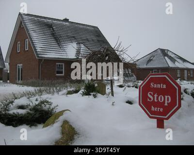 Un paesaggio innevato caratterizzato da una casa in mattoni con tetto inclinato. In primo piano, un segnale di stop rosso recita "Santa fermata qui", circondato da un b innevato Foto Stock
