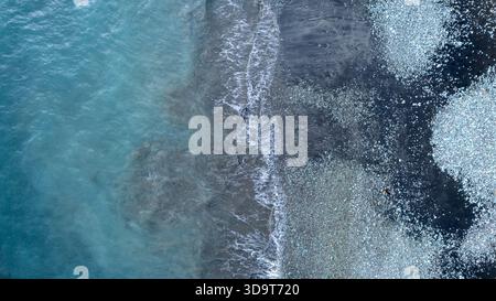 Una foto astratta dall'alto verso il basso con un drone che mostra il forte contrasto tra le acque cristalline dell'oceano turchese e la costa umida e scura Foto Stock