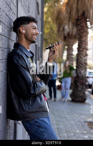 Adult African American man leaning against wall wearing jacket holding smartphone, copy space Foto Stock